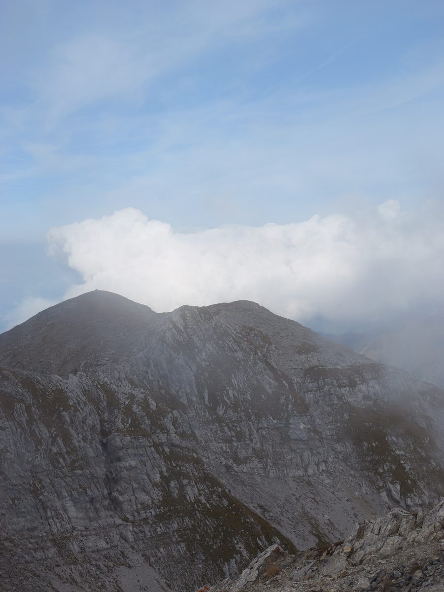 Bergkuppe unter blauem Himmel, eine einzelne Wolke liegt auf dem Gipfel