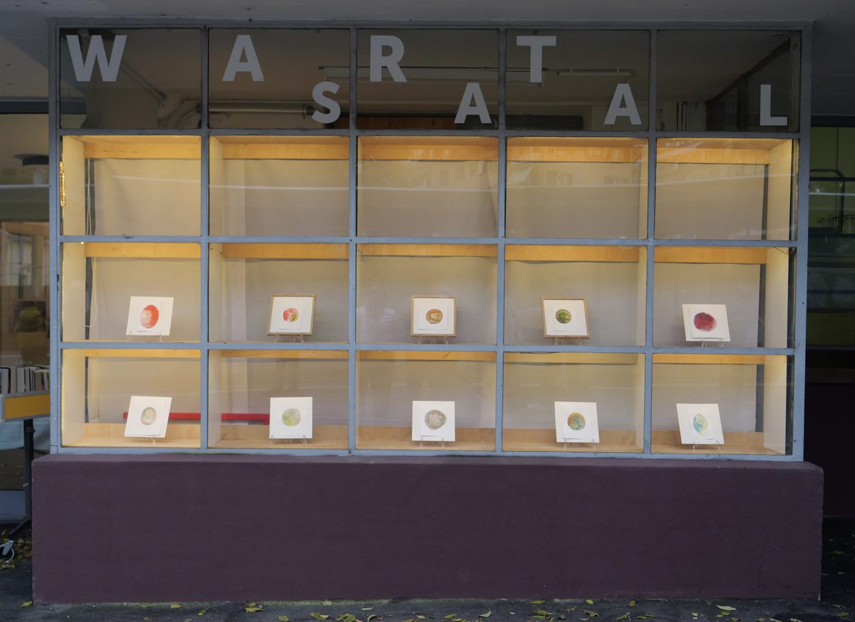 Beleuchtetes Schaufenster mit dem Schriftzug Wartsaal, darin zehn kleine Aquarelle in Fächern